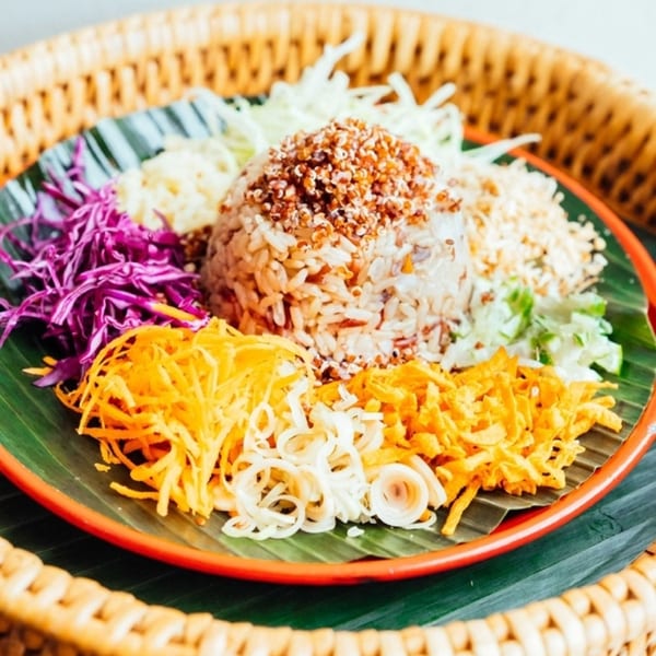 Thai rice dish with colorful shredded vegetables and crispy toppings on a banana leaf.