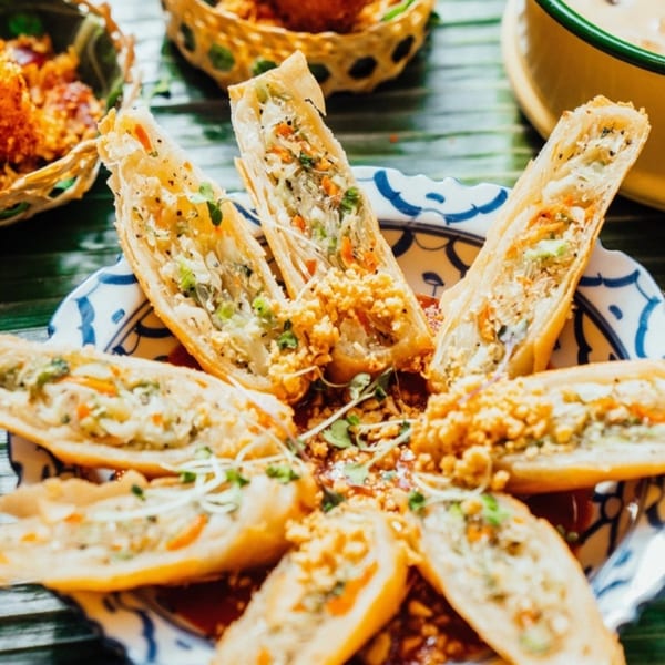 Crispy Thai spring rolls, cut in half, arranged on a decorative plate with sauce and garnish.