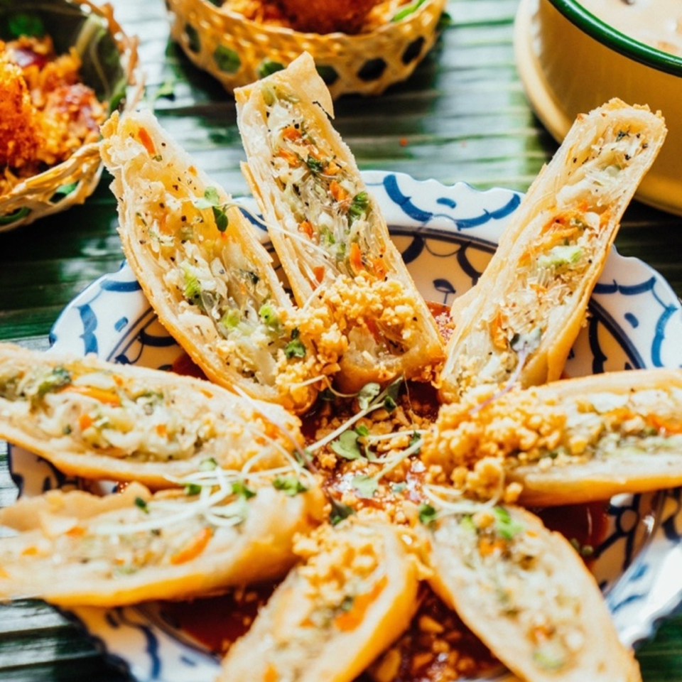 Crispy Thai spring rolls, cut in half, arranged on a decorative plate with sauce and garnish.