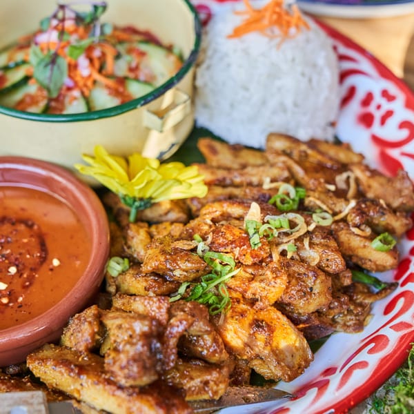 Grilled Thai chicken with peanut sauce, rice, and cucumber salad on a decorative tray.