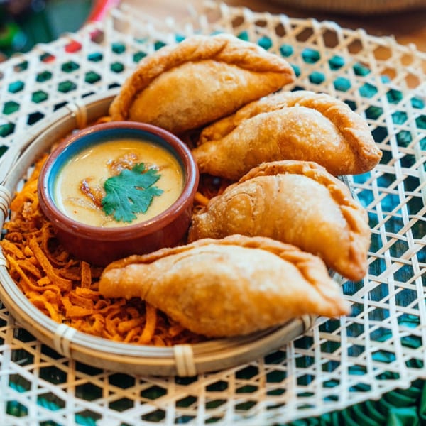 Golden-brown Thai curry puffs with a side of yellow dipping sauce and crispy noodles.