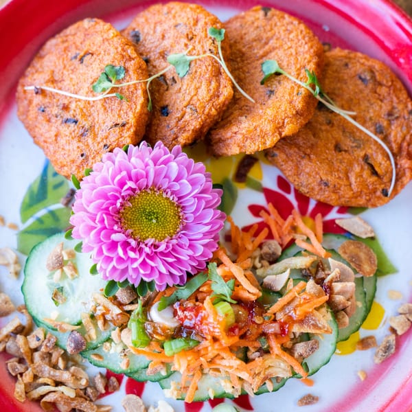 Daughter Thai Kitchen's fried fish cakes with cucumber, shredded carrots, and a pink flower garnish.