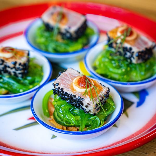 Four small bowls of Daughter Thai Kitchen's seared tuna with sesame seeds, seaweed salad, and sauce.