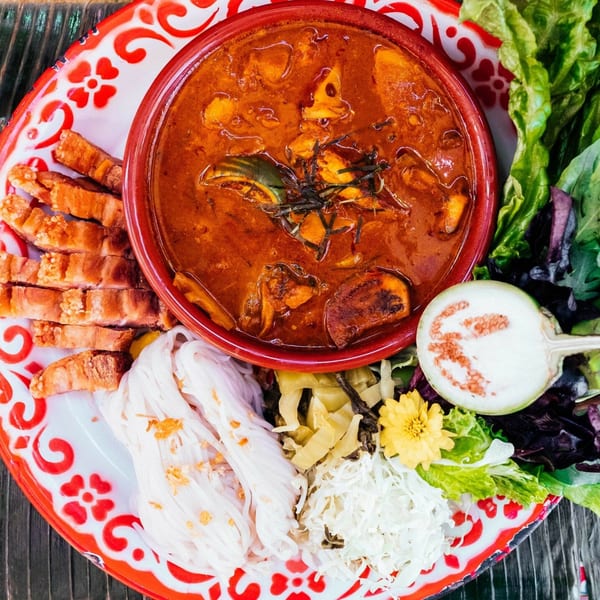 Daughter Thai Kitchen's red curry with crispy pork, noodles, fresh greens, and a sliced eggplant.